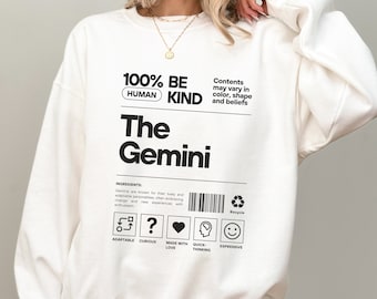 May include: White sweatshirt with black text that reads "100% Be Human Kind The Gemini". The text is styled to look like a product label with a barcode and icons that say "Adaptable", "Curious", "Made with Love", "Quick Thinking", and "Expressive".