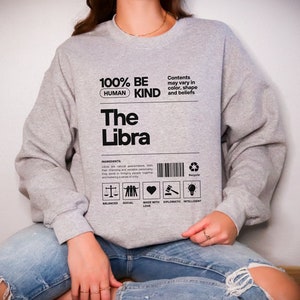 May include: Gray sweatshirt with black text that reads "100% Be Human Kind The Libra". The text is in a box with a barcode and symbols representing balanced, social, made with love, diplomatic, and intelligent.