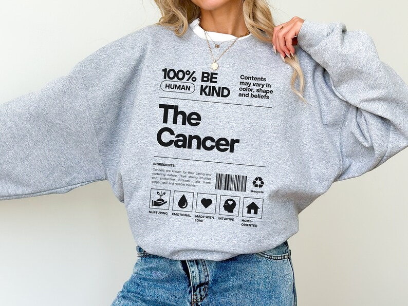 May include: Gray sweatshirt with the text "100% Human Be Kind The Cancer" and a label with icons and text that reads "Contents may vary in color, shape and beliefs".