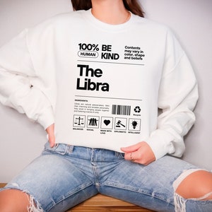 May include: White sweatshirt with black text that reads "100% Human Be Kind The Libra". The text is styled to look like a product label with a barcode and icons representing balanced, social, made with love, diplomatic, and intelligent.
