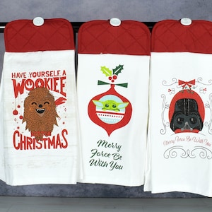 May include: Three white kitchen towels with red accents and Star Wars-themed designs. One towel says "Have Yourself a Wookiee Christmas," another features Baby Yoda in an ornament, and the third has Darth Vader. Each towel has a red quilted top.