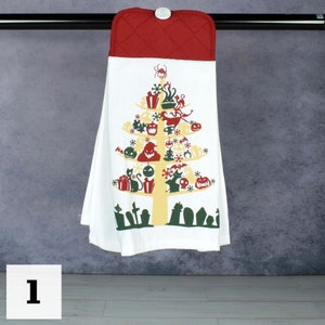 May include: A Halloween-themed tea towel with a white base and a tree-shaped design. The tree is decorated with spooky icons like pumpkins, bats, and ghosts. The top is a quilted red fabric with a button. The towel is hanging from a black bar.