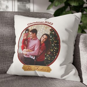 May include: White cushion featuring a family portrait within a red circular frame. The image shows a family of three in red and pink attire, set against a Christmas tree backdrop. Text includes "Christmas 2023" and "The Fisher's".