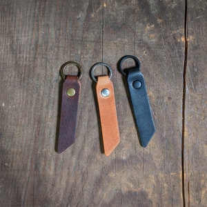 May include: Three leather keychains with metal rings. The keychains are brown, tan, and black.