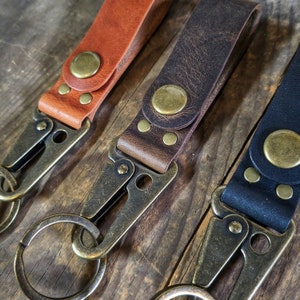 May include: Three leather keychains with antique brass key rings and swivel clips. The keychains are brown, dark brown, and black.