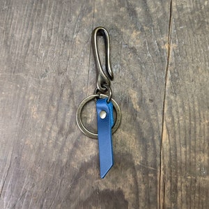 May include: A brass key chain with a blue leather strap and a ring. The key chain has a hook on the top.