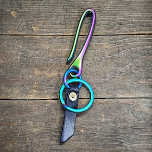 May include: A rainbow iridescent metal key hook with a black leather strap and two silver rings.