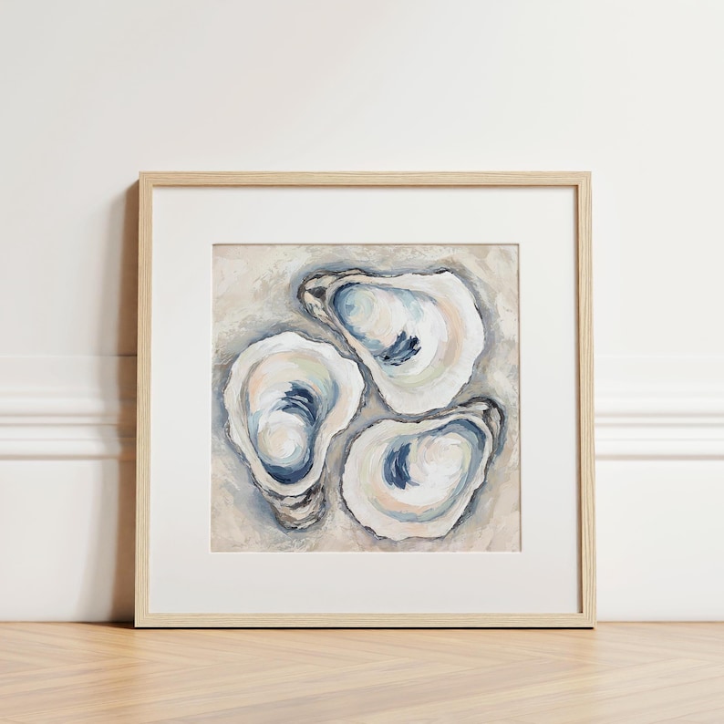 May include: A framed artwork featuring three oyster shells painted in shades of white, blue, and beige. The artwork is displayed in a light-colored wooden frame, adding a touch of coastal decor.