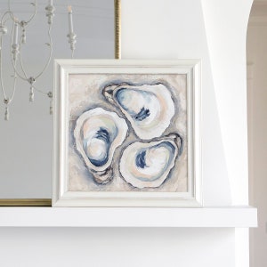 May include: Square framed artwork featuring an abstract painting of three oyster shells. The shells are painted in shades of white, blue, and beige, with visible brushstrokes. The artwork is displayed in a white frame.