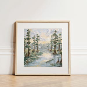 May include: A framed landscape painting depicting a serene swamp scene. The artwork features tall, slender trees with green foliage lining a calm waterway. The painting is in a light wood frame, adding a natural touch to the artwork.