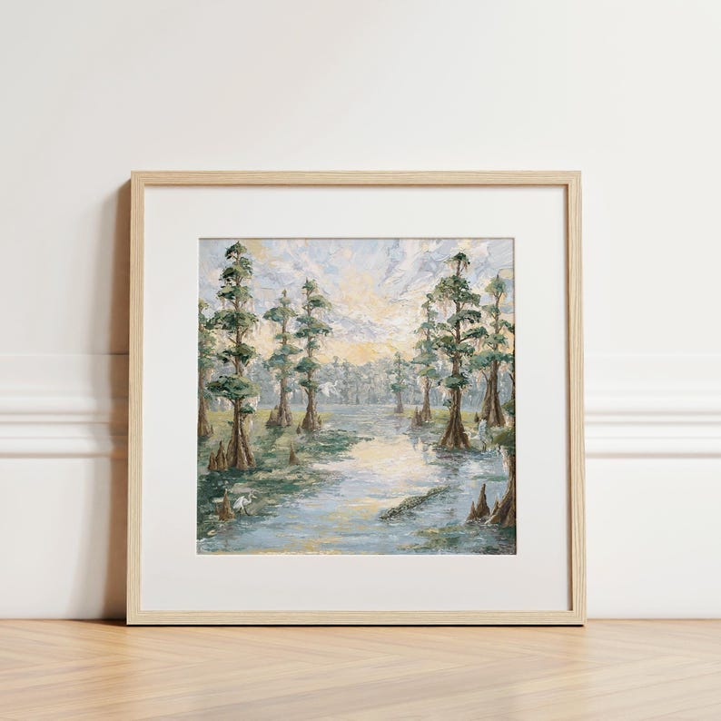 May include: A framed landscape painting depicting a serene swamp scene. The artwork features tall, slender trees with green foliage lining a calm waterway. The painting is in a light wood frame, adding a natural touch to the artwork.