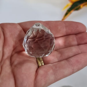 May include: A clear crystal ball with a faceted design, held in a hand.