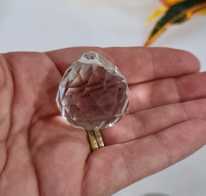 May include: A clear crystal ball with a faceted design, held in a hand.