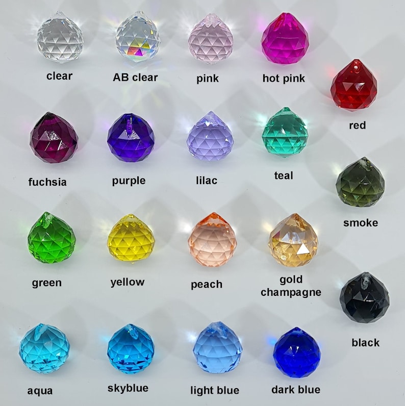 May include: A collection of faceted crystal pendants in various colors, including clear, pink, red, purple, green, yellow, and blue. Each pendant has a small hole for hanging and is labeled with its color name.