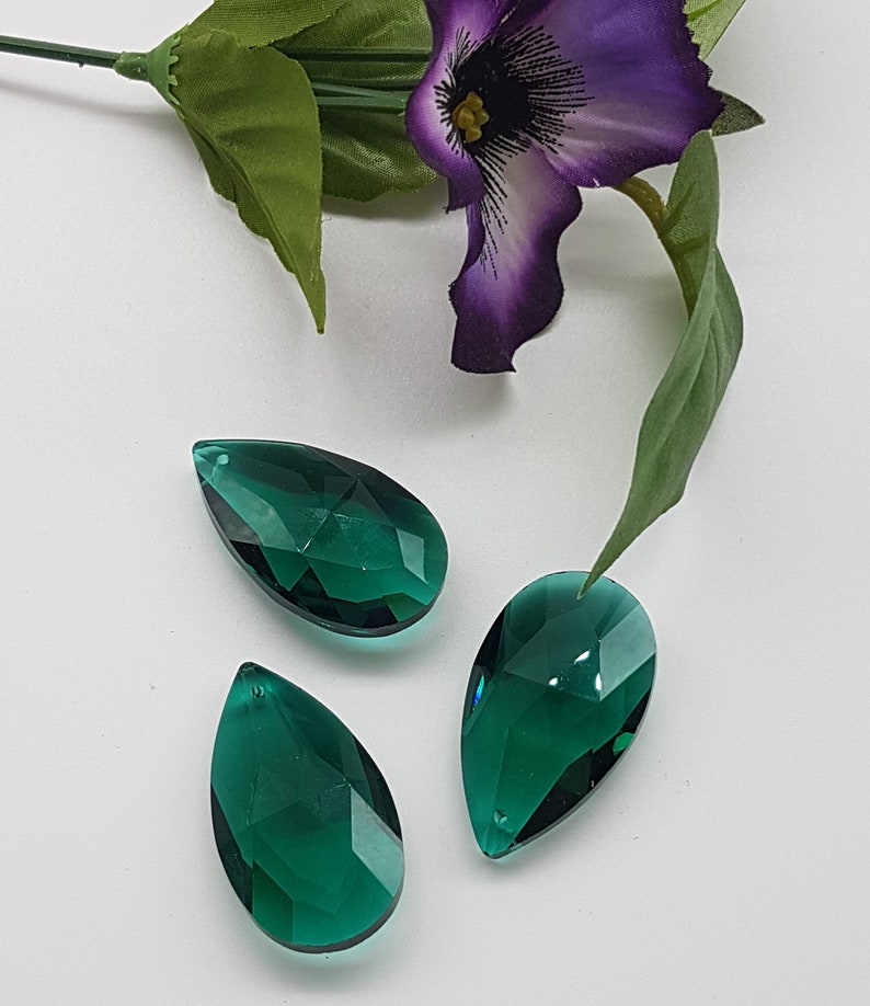 May include: Three teardrop-shaped crystal prisms in a deep emerald green color. The prisms are faceted and reflect light.