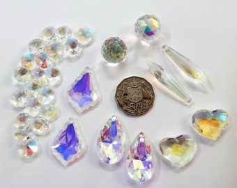 Puede incluir: Un surtido de cuentas y colgantes de cristal iridiscente en varias formas, incluyendo esferas, lágrimas y corazones. Los cristales reflejan un arcoíris de colores. Se incluye una moneda de 50 centavos como referencia de tamaño.