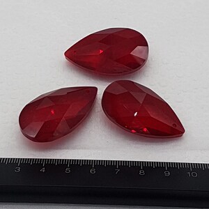 May include: Three red crystal teardrop shaped pendants. The pendants are faceted and have a shiny finish.