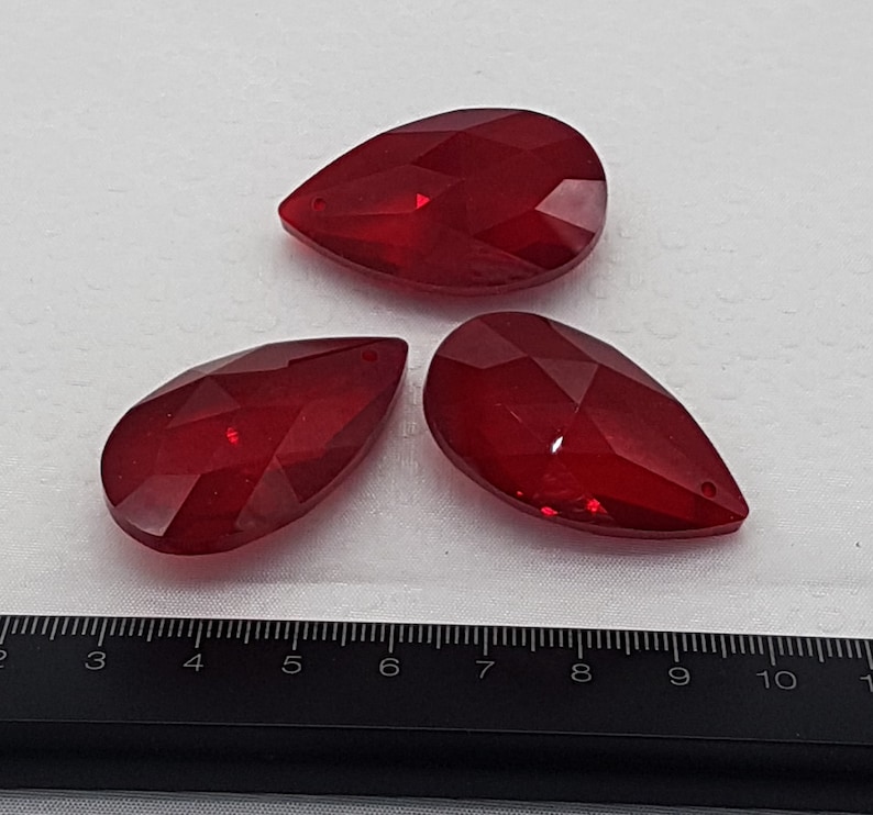 May include: Three red crystal teardrop shaped pendants. The pendants are faceted and have a shiny finish.