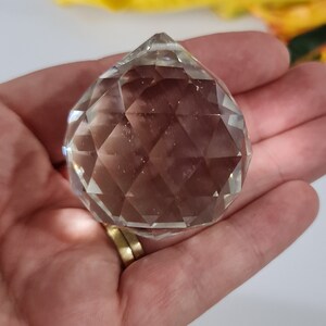 May include: A clear crystal ball with many facets, held in a hand.