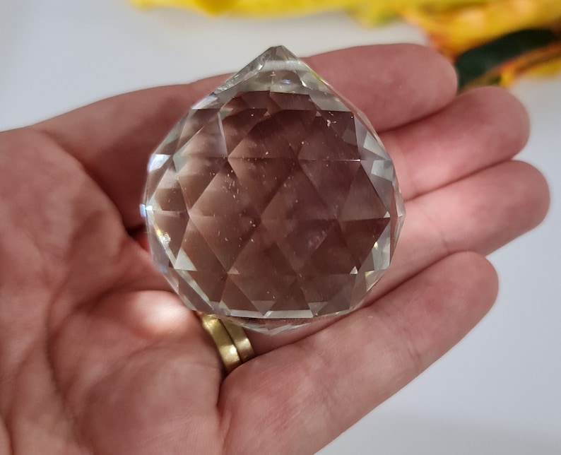 May include: A clear crystal ball with many facets, held in a hand.