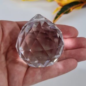 May include: A clear crystal ball with a faceted design. The ball is about 2 inches in diameter and is held in a hand.