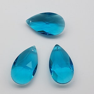 May include: Three teardrop-shaped crystal prisms in a vibrant turquoise blue color. The prisms are faceted and have a hole at the top for hanging.