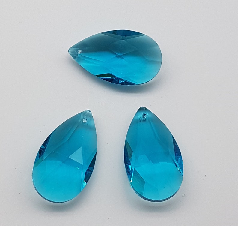 May include: Three teardrop-shaped crystal prisms in a vibrant turquoise blue color. The prisms are faceted and have a hole at the top for hanging.