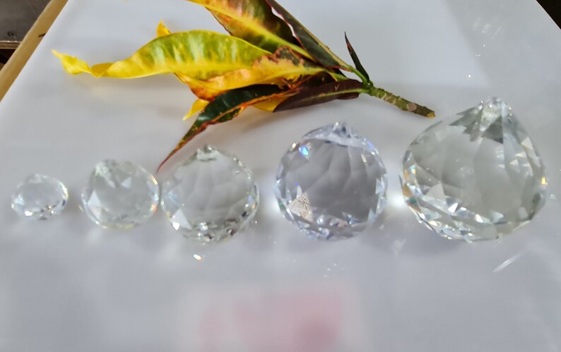 May include: Five clear crystal prisms of varying sizes, arranged in a row from smallest to largest on a white surface.
