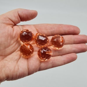 May include: Five small, round, faceted beads in a translucent peach-orange color. Each bead features a geometric cut surface that reflects light, creating a sparkling appearance. The beads are spherical with a small hole for threading.