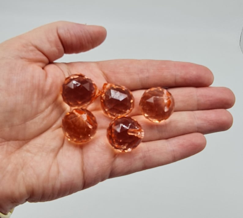 May include: Five small, round, faceted beads in a translucent peach-orange color. Each bead features a geometric cut surface that reflects light, creating a sparkling appearance. The beads are spherical with a small hole for threading.