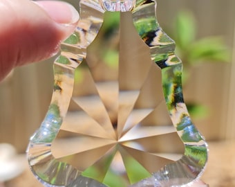 Puede incluir: Un prisma de cristal transparente con un diseño facetado y un borde festoneado. El prisma tiene forma de lágrima y tiene un agujero en la parte superior para colgarlo.