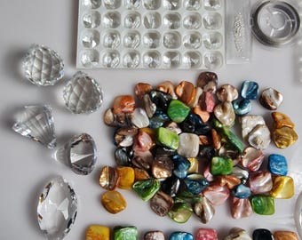 May include: Assortment of colorful iridescent shell beads and clear glass beads in various shapes and sizes. The beads are arranged on a white surface. There is also a clear plastic container with small clear glass beads.