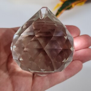 May include: A clear crystal prism ball with a faceted design. The ball is approximately 2 inches in diameter and has a small hole at the top for hanging.