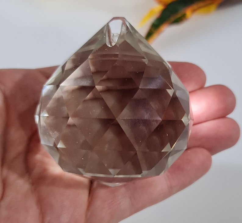 May include: A clear crystal prism ball with a faceted design. The ball is approximately 2 inches in diameter and has a small hole at the top for hanging.