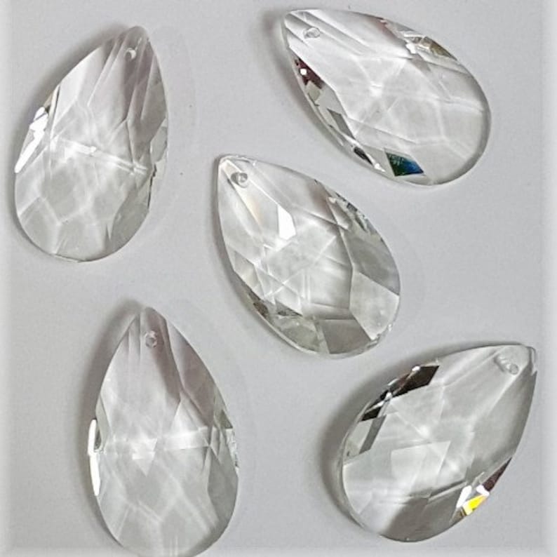 May include: Five clear glass teardrop-shaped crystal prisms with a hole at the top for hanging.