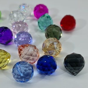 May include: A collection of multi-colored, faceted crystal beads in various hues including red, blue, green, yellow, purple, pink, and clear. Each bead features a geometric, multi-faceted surface that reflects light, creating a sparkling appearance.