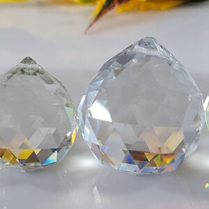 May include: Four clear glass crystal prisms of varying sizes, hanging from a ceiling or chandelier. The prisms are faceted and reflect light, creating rainbows.