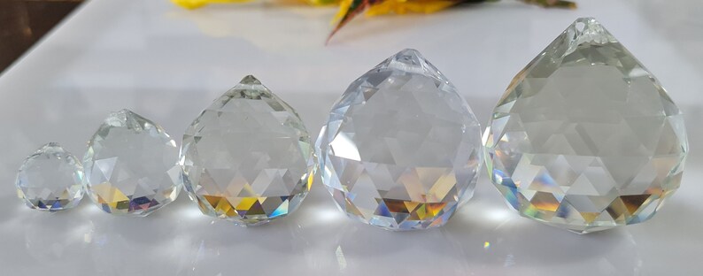 May include: Four clear glass crystal prisms of varying sizes, hanging from a ceiling or chandelier. The prisms are faceted and reflect light, creating rainbows.