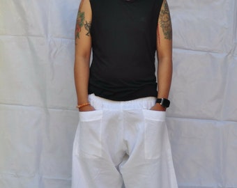 May include: A person wearing a black sleeveless shirt and white pants with large pockets. The person has tattoos on their arms.