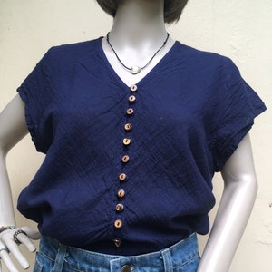 May include: A navy blue short-sleeved button-down shirt with wooden buttons. The shirt is worn over a pair of blue denim jeans with a button fly.