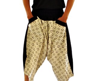 May include: A person wearing black sleeveless shirt and beige pants with a black and white geometric pattern. The pants have a drawstring waist and pockets on the sides.