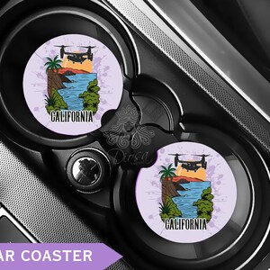 May include: Two car coasters with a California design. Each coaster features a landscape with a helicopter, palm tree, ocean, and the word "CALIFORNIA" in black text. The coasters are set in a car's cup holders.