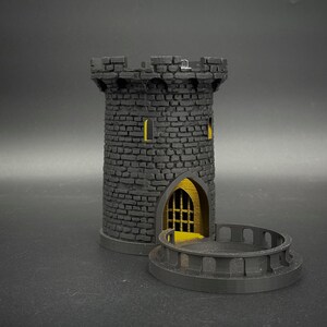 Könnte beinhalten: Ein schwarzer 3D-gedruckter Turm mit einer gelben Tür und Fenstern. Der Turm hat einen Balkon mit einem Geländer. Der Turm ist ein Würfelturm für Brettspiele.