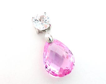 May include: A pendant featuring a round, clear, faceted stone set in silver-toned metal above a larger, pear-shaped, faceted pink stone. The two stones are connected by a small silver-toned metal bail, creating a dangling, multi-stone design.