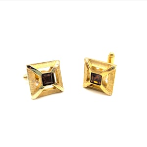 May include: A pair of gold-toned cufflinks with a square design. Each cufflink features a textured frame with a dark brown square center stone. The cufflinks are set against a white background.