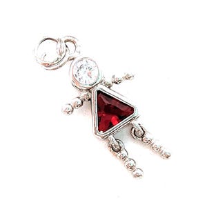 Peut inclure: Un charm argenté en forme de personnage avec une pierre ronde transparente à facettes pour la tête et une pierre triangulaire rouge foncé à facettes pour le corps. Les bras et les jambes sont faits de petites perles argentées, avec un anneau au sommet.