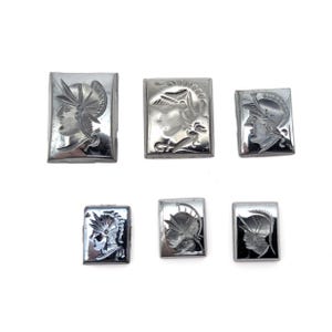 May include: Six rectangular, silver-toned metal buttons. Each button features a profile of a person wearing a helmet, possibly a Roman or Greek soldier. The buttons are arranged on a white background.