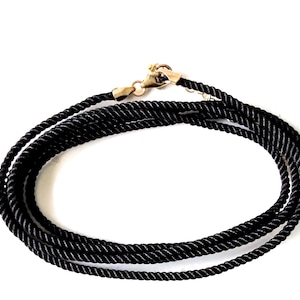 May include: A black cord necklace featuring a twisted rope texture and a gold-toned metal lobster claw clasp. The cord is coiled in a circular shape, showcasing the consistent thickness of the material and the metallic finish of the hardware.