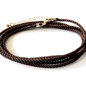 Pode incluir: Um colar de cordão castanho escuro com uma textura de corda torcida. O colar inclui um fecho de lagosta em metal dourado e uma corrente extensora ajustável com uma pequena conta redonda na extremidade para um ajuste seguro.