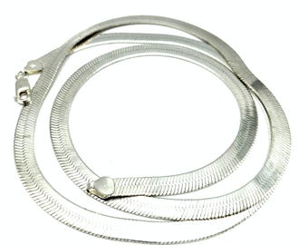 Puede incluir: Un collar de cadena de espiga en tono plateado con un diseño de eslabones planos y flexibles con un acabado metálico pulido. El collar incluye un cierre de mosquetón seguro y una pequeña etiqueta en forma de corazón cerca del cierre.